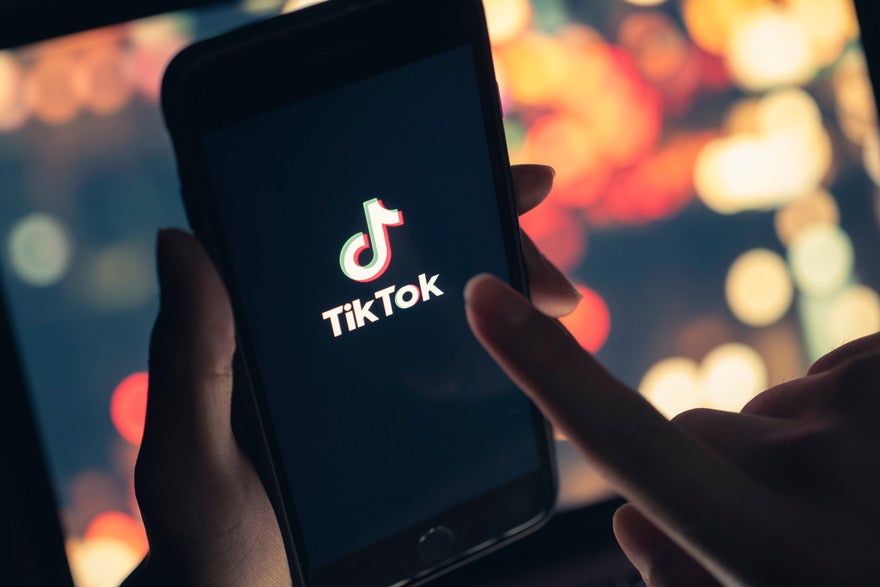 AdobeStock_432394124_Editorial_Use_Only (1) Hands holding a mobile device showing the TikTok logo on screen