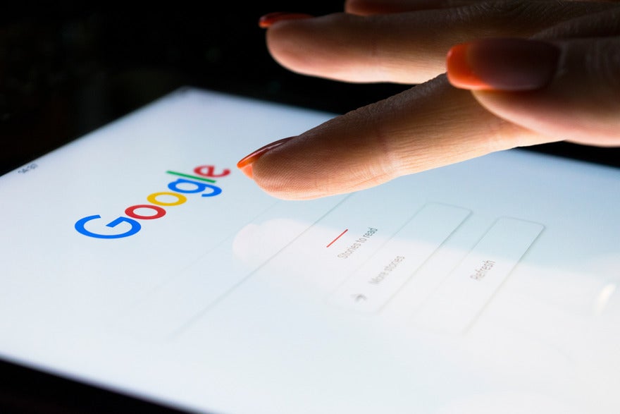 Google illegal monopoly Person tapping a tablet device with the Google homepage on screen
