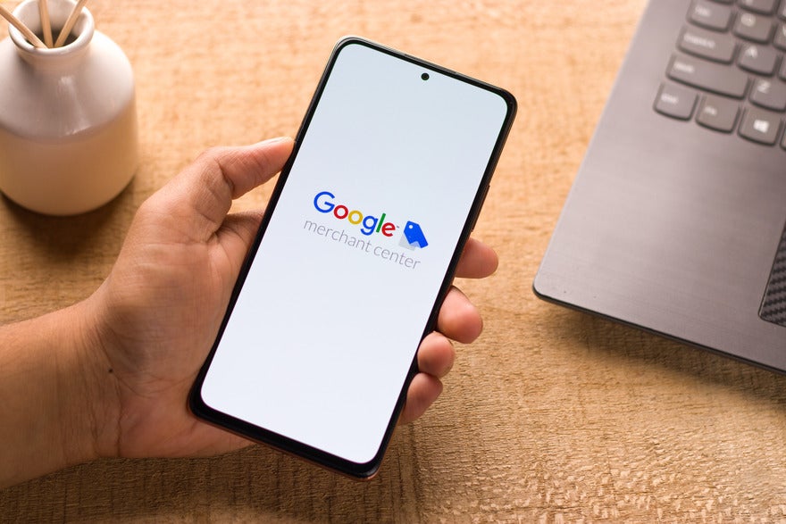 Google merchant center Hand holding a mobile with Google merchant center logo displayed on a white screen