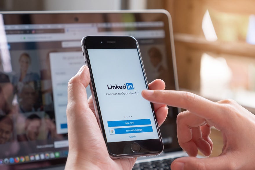 LinkedIn Newsletter Upgrade Person holding a mobile device with the LinkedIn login page on the screen