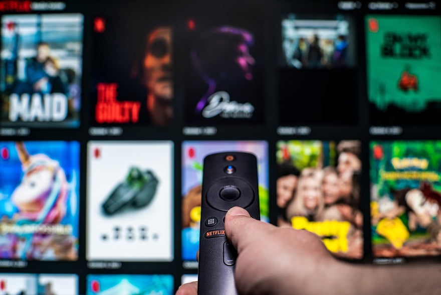 Netflix TV app Blurred image of Netflix's content with a hand holding a TV remote pointing at the screen