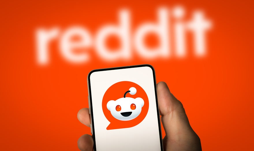 Reddit Google partnership Hand holding a mobile showing a white background with the Reddit logo on, held against the red Reddit background