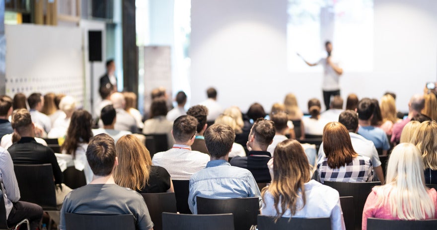 SEO conferences in USA Audience of people sat in chairs listening to a speaker deliver a talk at a conference event