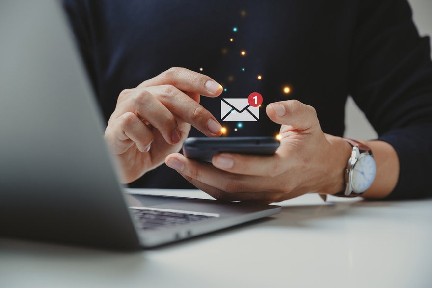 SEO newsletters Person holding a mobile phone with a symbol for a new email floating above the device