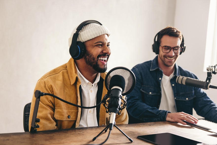 SEO podcast Two men sat a desk with podcast equipment in front of them and headphones on